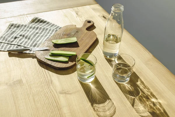 Vue aérienne des concombres coupés sur le panneau en bois et des verres avec de l'eau de désintoxication sur la surface en bois — Photo de stock