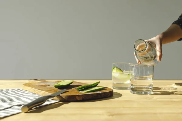 Cropped image of woman pouring water into glasses with cucumbers — Stock Photo