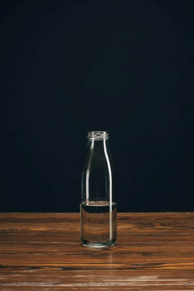 Botella de vidrio con agua mineral en la mesa marrón en negro - foto de stock