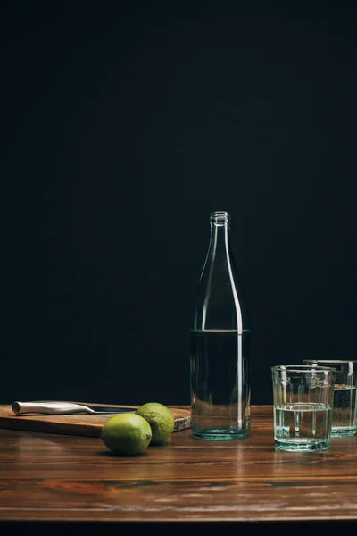 Bottle and glasses with water and limes on brown table — Stock Photo