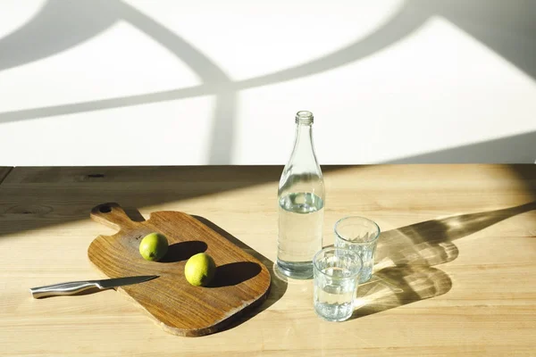 Eau minérale et citrons verts pour préparer la limonade sur une table en bois — Photo de stock