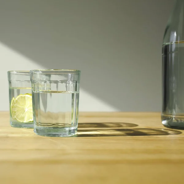 Vasos con agua de desintoxicación con limas sobre mesa de madera - foto de stock