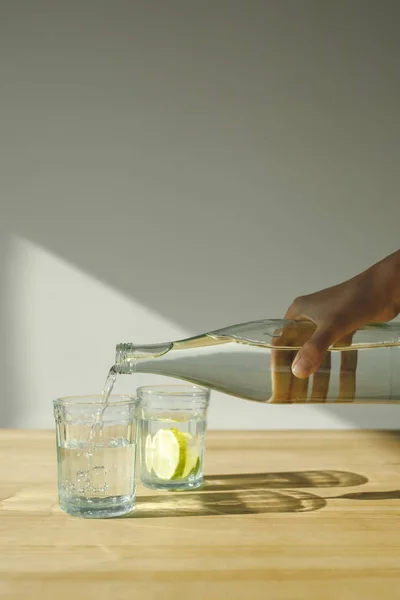 Imagen recortada de la mujer vertiendo agua de la botella en vidrio transparente - foto de stock