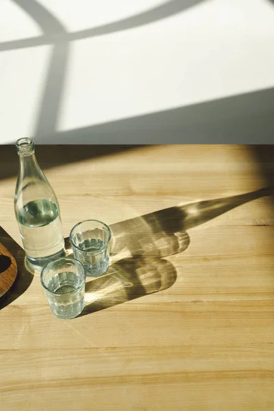 Vista aerea di bottiglia trasparente e bicchieri con acqua minerale — Foto stock