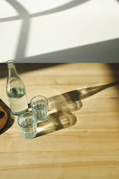 Overhead view of transparent bottle and glasses with mineral water — Stock Photo