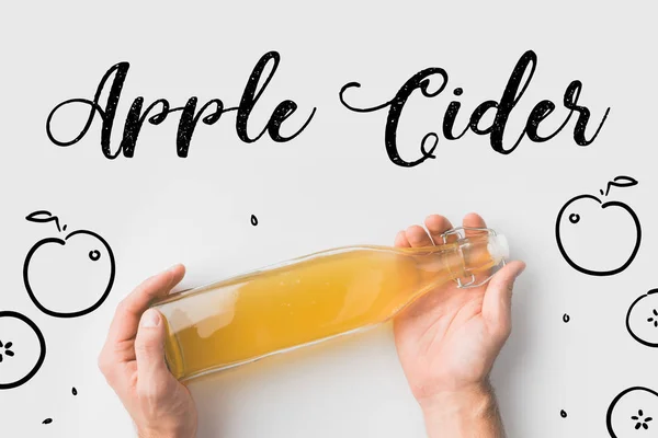 Vista superior de la persona que sostiene la botella de sidra con manzanas dibujadas a mano y letras en la superficie blanca — Stock Photo