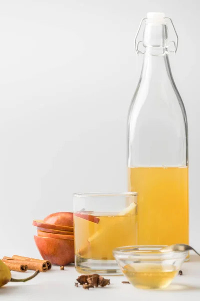 Apple cider in bottle and glass with spices on white surface — Stock Photo