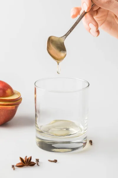 Plan recadré de la femme versant du miel dans le verre de cuillère sur table blanche — Photo de stock