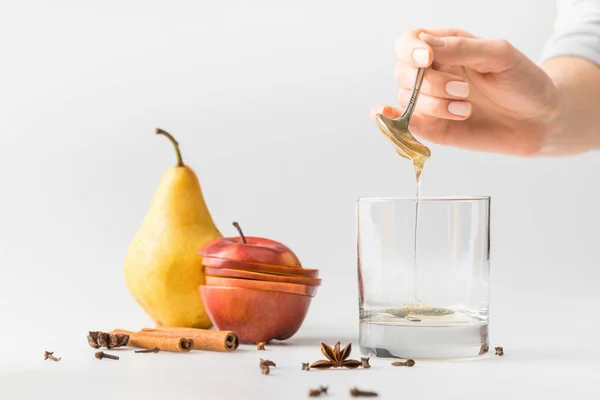 Cropped shot of woman pouring honey in glass from spoon on white table — Stock Photo