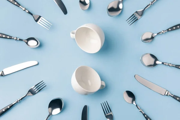 Top view of tea cups surrounded by flatware isolated on blue — Stock Photo