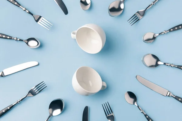 Vista superior de tazas de té rodeadas de cubiertos aislados en azul - foto de stock