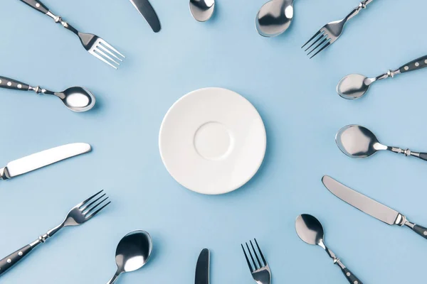 Top view of plate surrounded by flatware isolated on blue — Stock Photo