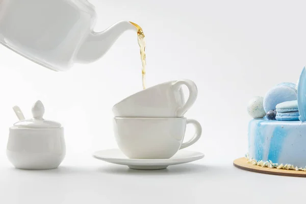 Tetera verter el té en tazas cerca de pastel azul aislado en blanco - foto de stock