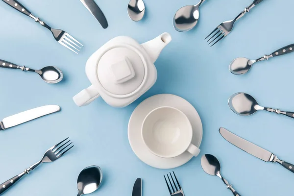 Верхний вид чайник с чашкой на тарелке, в окружении столовых приборов изолированы на синий — стоковое фото