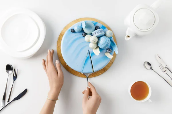 Draufsicht der abgeschnittenen Hände beim Aufschneiden von Kuchen auf Schneidebrett isoliert auf Weiß — Stockfoto