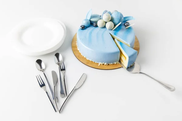 Blue tasty cake on chopping board with cake server and plates isolated on white — Stock Photo
