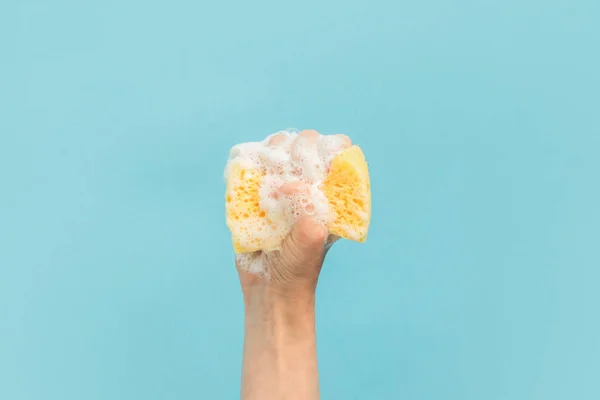 Vista recortada de la mano que sostiene la esponja de lavado con espuma, aislada en azul - foto de stock