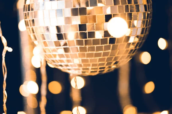 Close-up shot of glossy disco ball on black background with garland hanging around — Stock Photo