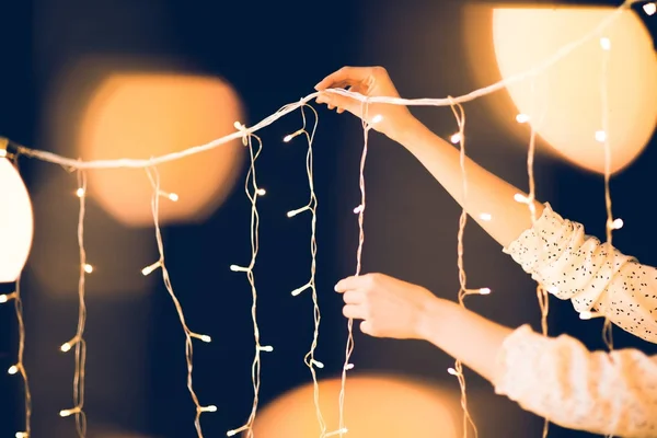 Recortado tiro de mujer colgando hermosa guirnalda de Navidad sobre fondo negro - foto de stock