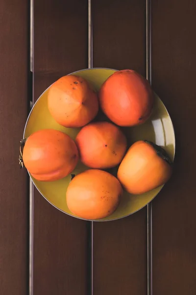 Top view of yellow plate with orange persimmons — Stock Photo