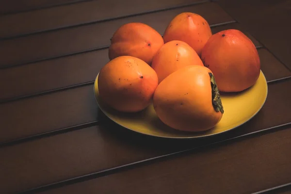 Placa amarilla con caquis naranjas sobre mesa marrón - foto de stock
