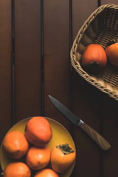 Draufsicht auf Strohkorb und Teller mit Kaki und Messer auf dem Tisch — Stockfoto