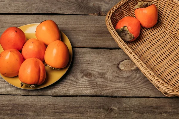 Ripe persimmons on plate and in straw basket — Stock Photo