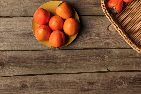 Top view of appetizing persimmons on plate and in basket on table — Stock Photo