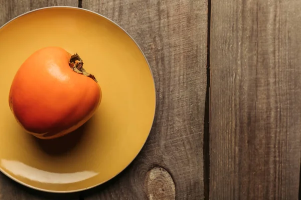 Top view of persimmon on yellow plate on wooden surface — Stock Photo