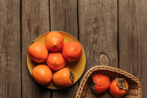 Vue de dessus de délicieux kaki sur l'assiette et dans le panier sur la table — Photo de stock