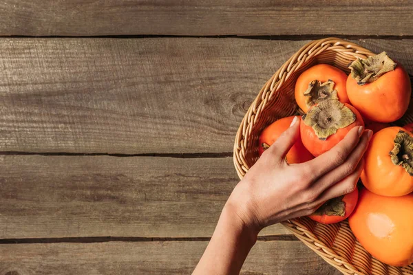 Abgeschnittenes Bild einer Frau, die Persimmon aus einem Strohkorb nimmt — Stockfoto