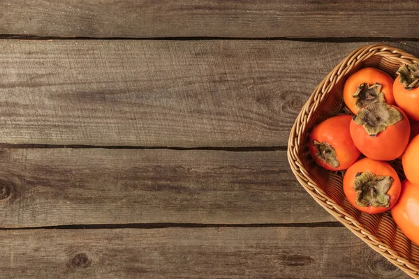 Vue du dessus du panier de paille avec des kaki mûrs sur une table en bois — Photo de stock