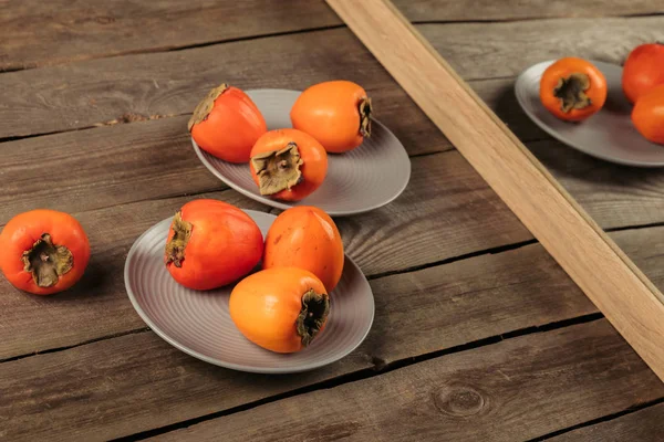 Reife Persimmons auf Tellern, die sich im Spiegel spiegeln — Stockfoto