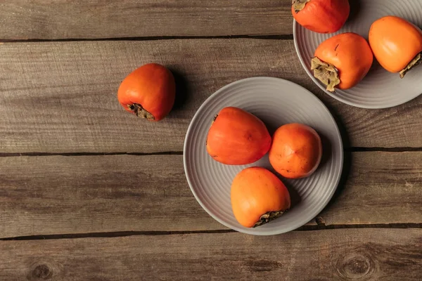 Top view of persimmons on plates on wooden table — Stock Photo