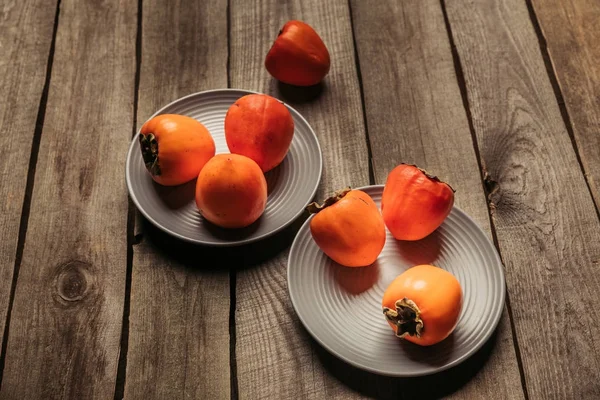 Спелые апельсиновые хурмы на тарелках на сером деревянном столе — стоковое фото