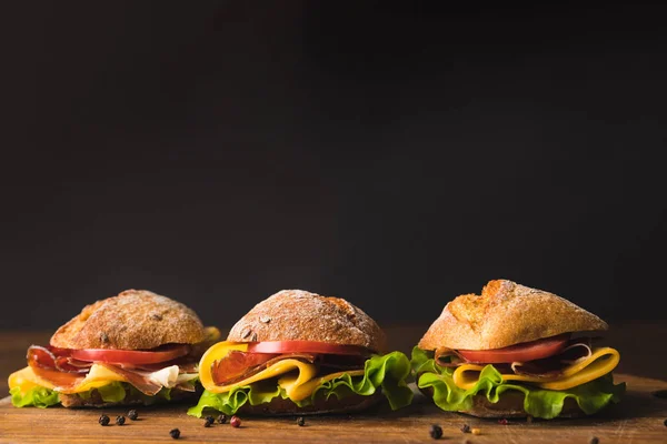 Sandwiches with cheese and vegetables on wooden board with scattered pepper — Stock Photo