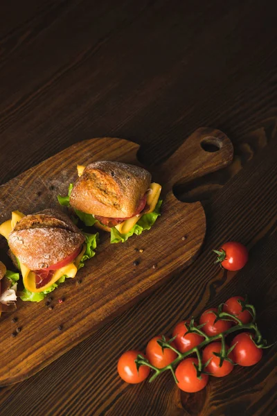 Vue aérienne des sandwichs au fromage sur plateau en bois et des tomates cerises sur table — Photo de stock