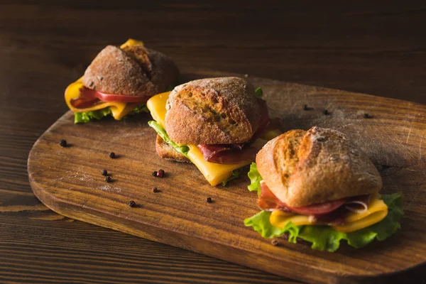 Trois sandwichs au fromage et légumes sur planche à découper — Photo de stock