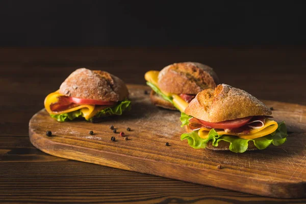 Three sandwiches with cheese and vegetables on wooden board — Stock Photo