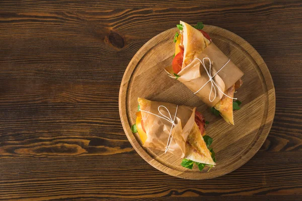 Vista superior de dos deliciosos panini en tabla de cortar en mesa de madera - foto de stock