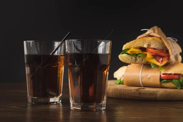 Dois copos de cola na mesa e panini na tábua de madeira — Fotografia de Stock