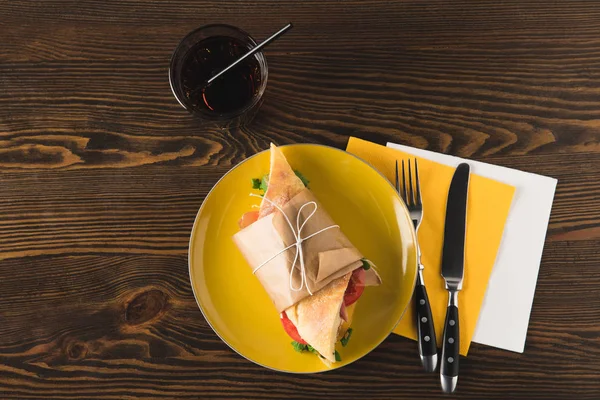 Top view of panini on yellow plate with fork and knife on napkins — Stock Photo