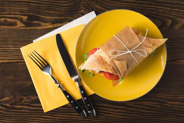 Top view of panini on yellow plate with fork and knife — Stock Photo