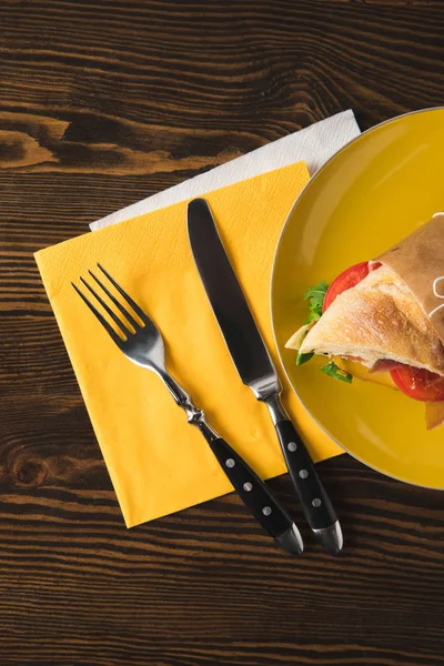 Vue du dessus du sandwich sur plaque jaune avec fourchette et couteau — Photo de stock