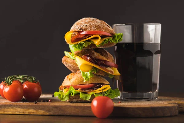 Big sandwich with cherry tomatoes and glass of cola on cutting board — Stock Photo