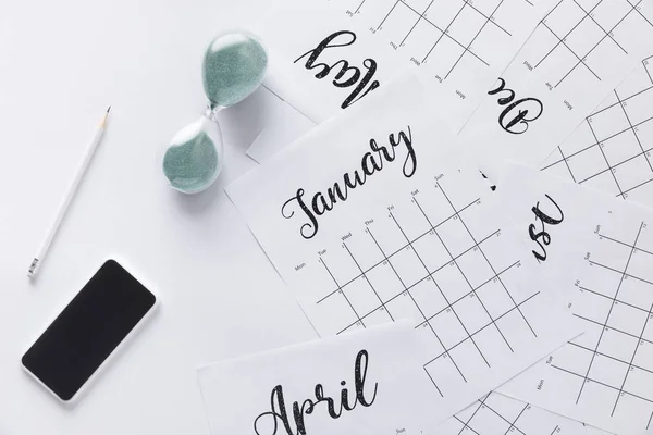 Pose plate avec calendrier, smartphone, crayon et horloge de sable isolé sur blanc — Photo de stock