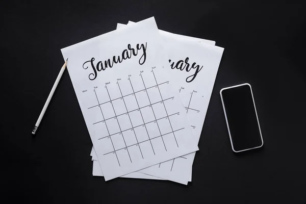 Pose plate avec calendrier en papier, smartphone et crayon isolé sur noir — Photo de stock