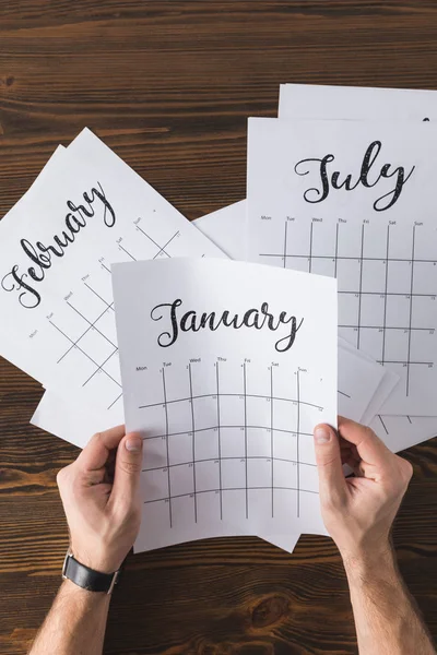 Vista parcial del hombre sosteniendo el calendario en las manos en la mesa de madera - foto de stock