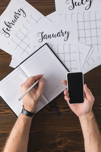 Partial view of businessman making notes in notebook at table with calendar — Stock Photo