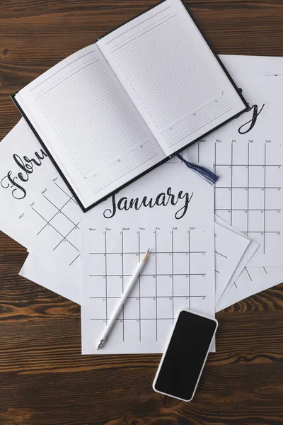 Pose plate avec bloc-notes vide, calendrier, crayon et smartphone sur la surface en bois — Photo de stock